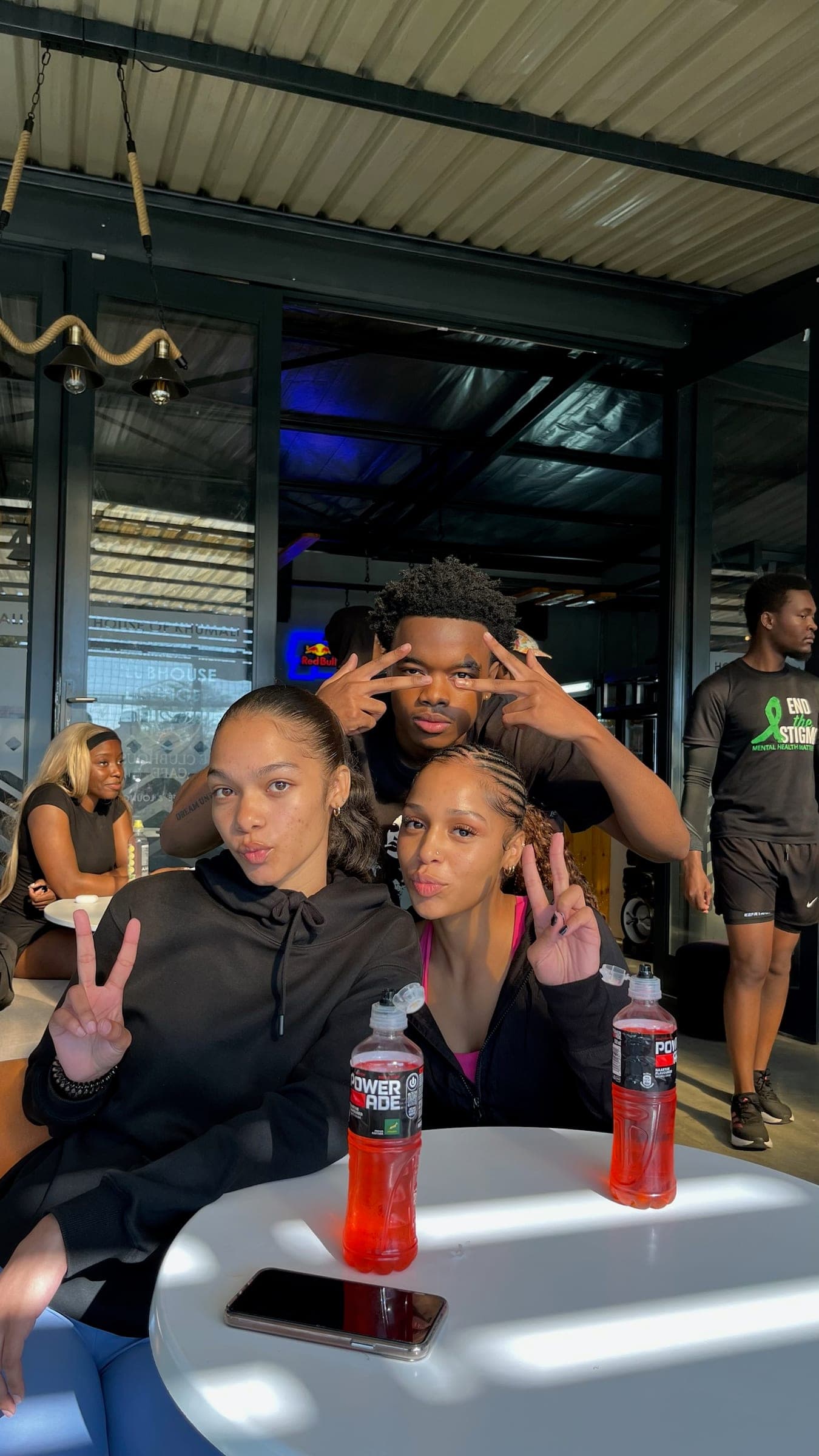 Three members throwing peace signs around a clubhouse table with cold drinks