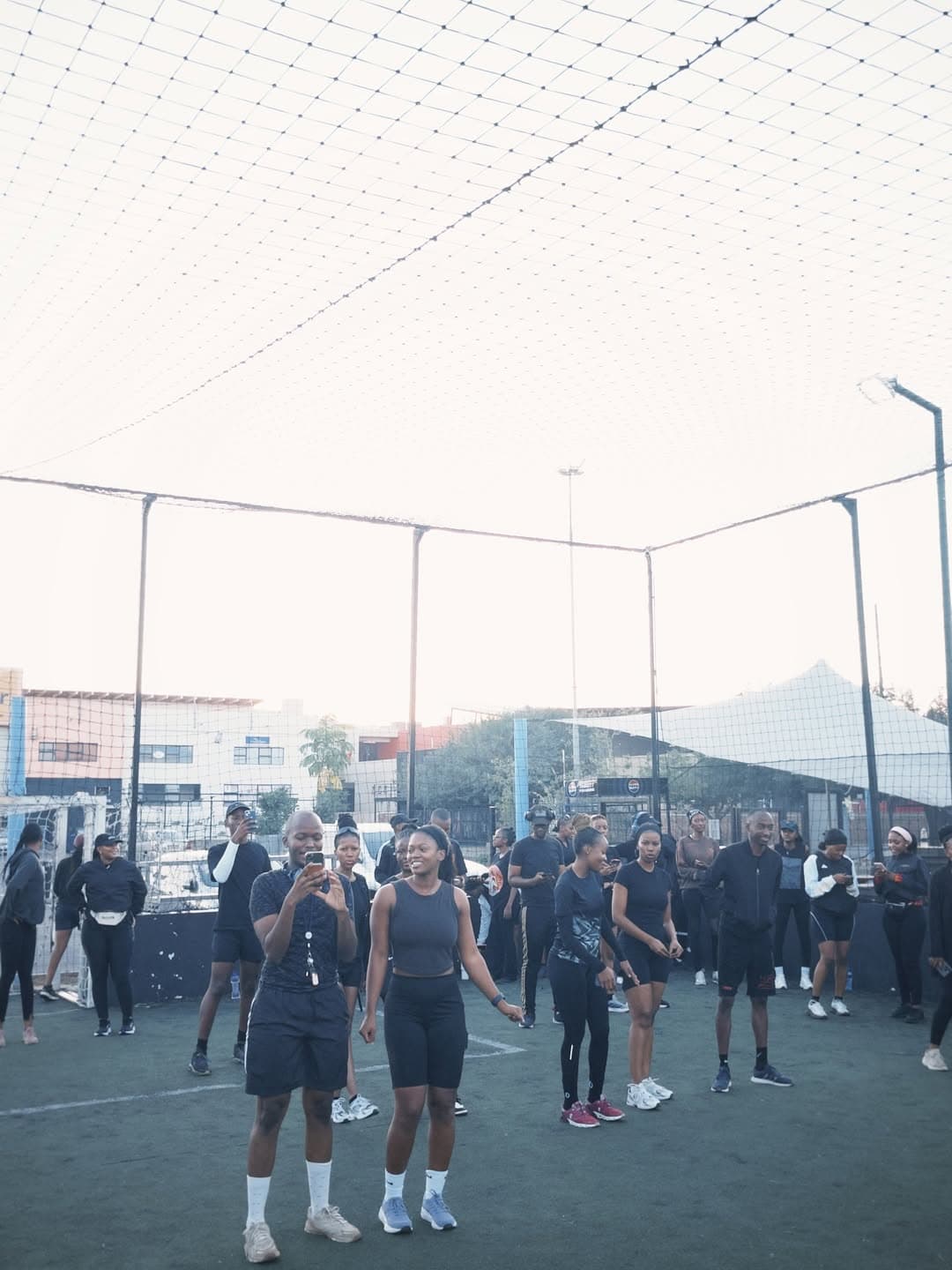 Large group of Pace Us runners gathered under the netted pitch before a Saturday run