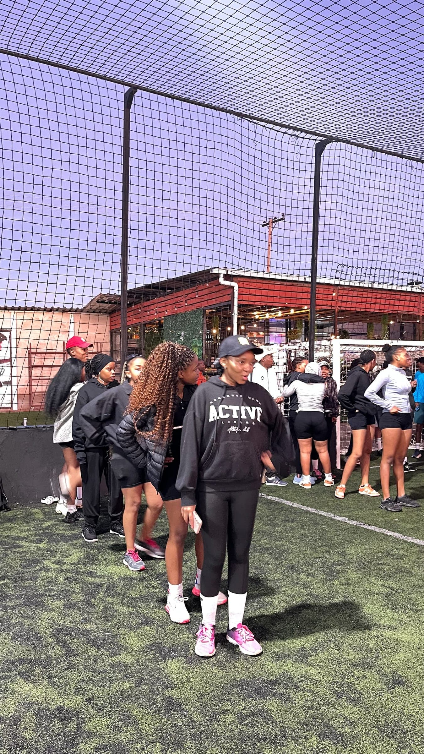Runners waiting on the turf pitch before the start, one in a Pace Us hoodie