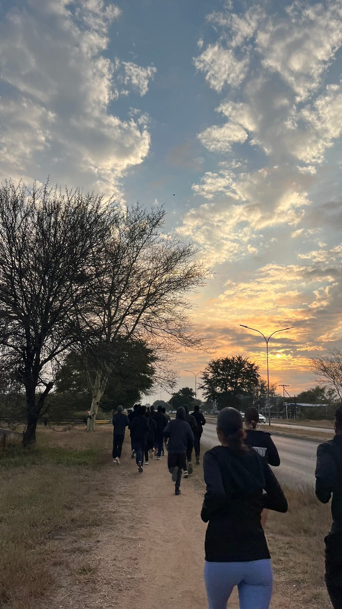 Pace Us runners strung out single file along a dirt path at sunrise